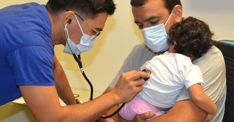 A clinician checks on a child being held by their parent