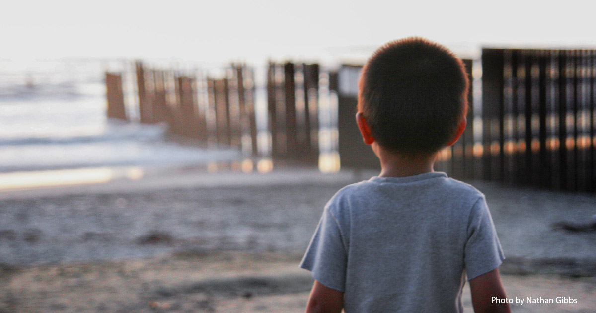 A child stands looking at the wall on the Mexican border